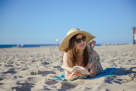 一个年轻的黑发女人在沙滩上放松、看书的画像