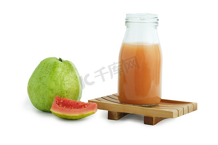 切片水果摄影照片_新鲜番石榴汁放在木杯垫上方的瓶玻璃上，上面放着生水果和切片水果