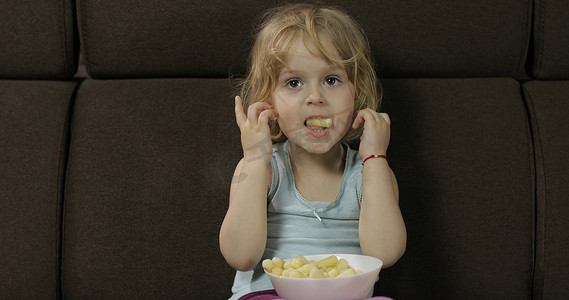 女孩坐在沙发上吃玉米泡芙。