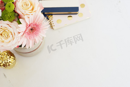 粉色菠萝摄影照片_平躺风格的女性工作场所概念，有鲜花、金菠萝、白色大理石背景的笔记本。