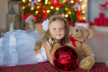 年轻漂亮的女孩穿着蓝白色优雅的晚礼服坐在圣诞树附近的地板上，并在新年前夜礼物。