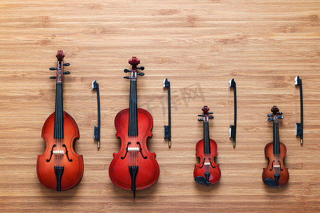 古典背景摄影照片_一套四件玩具弦乐管弦乐器：小提琴、大提琴、低音提琴、木制背景中的中提琴。