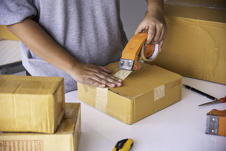 包裹快递的摄影照片_工作人员正在用胶带将包裹货物打包发往客户