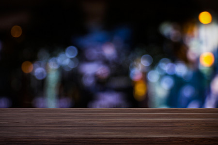 模糊的咖啡厅餐厅或咖啡店空荡荡的深色木桌，带有模糊的浅金色散景抽象背景，用于蒙太奇产品展示或设计。