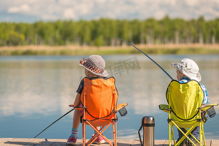 卡通男孩坐在西瓜上摄影照片_带钓鱼竿的孩子们坐在木码头上钓鱼