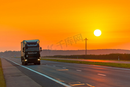 朝阳摄影照片_卡车在黎明时分在朝阳的光芒下行驶在高速公路上