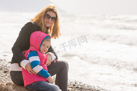 我和春天摄影照片_我妈妈和五岁的女儿坐在沙滩上，看着旋转架
