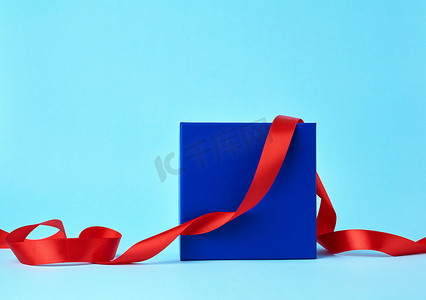 礼物的方形的蓝色纸板箱和被扭曲的丝绸红色丝带