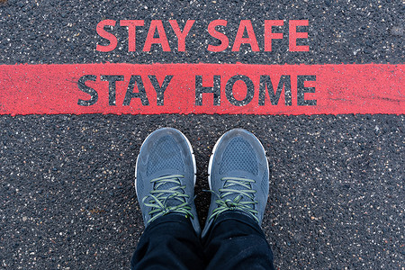 safe摄影照片_穿着运动鞋的男人站在红线旁边，上面写着 STAY SAFE，