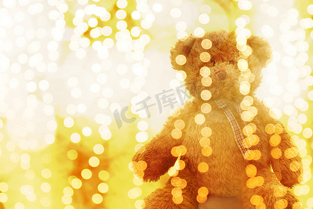 泰迪熊娃娃在灯光线散景金色明亮的圣诞节或新年快乐背景，闪闪发光的金黄色背景中的熊模糊散景明亮（选择性聚焦）