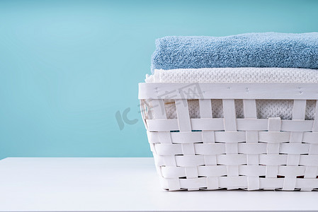 叠衣服摄影照片_蓝色背景中白色洗衣篮中的一叠干净毛巾