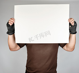 五一大放价摄影照片_穿着棕色衣服的运动员拿着一大张空白的白纸