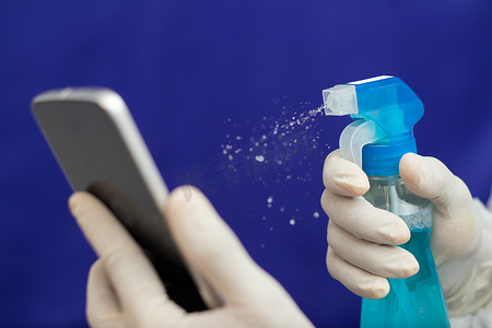 医生清洁手机以消除 Covid-19 — 护士手戴手套在医院用液体消毒剂清洁手机 — 酒精擦拭冠状病毒污染