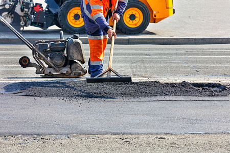在道路设备的背景下，一名道路工人正在路段上平整新沥青。