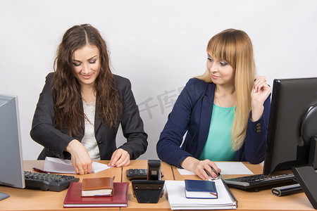 两个在办公室工作的年轻女性，一个放一张纸，第二个惊讶地盯着她