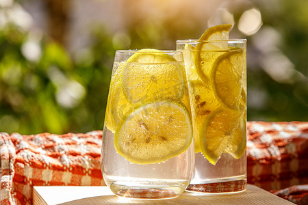 柠檬水摄影照片_在花园背景的玻璃杯中加新鲜柠檬的柠檬水。