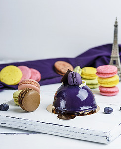 马卡龙背景板摄影照片_白色木板上的淡紫色圆蛋糕和马卡龙