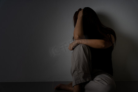 女人哭泣摄影照片_悲伤的女人独自坐在黑暗的房间里抱着膝盖哭泣。