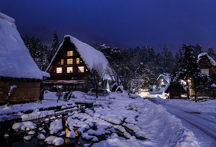 黄昏的村庄摄影照片_夜间树林旁历史悠久的村庄被雪覆盖的日本农舍