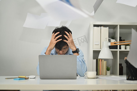 压力重重的男办公室职员对工作截止日期感到苦恼焦虑，坐在办公桌前，文书工作掉落