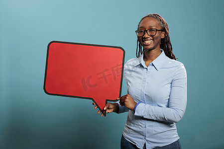 非洲裔美国自信、笑容满面的女人拿着蓝色背景的红色纸板语音气泡。