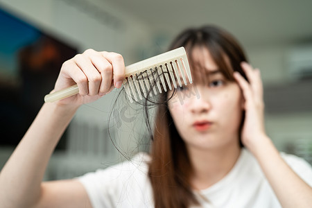 梳子摄影照片_亚洲女性有长脱发问题，头发附着在梳子上。