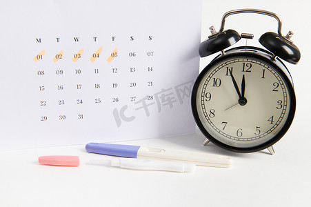 阳性喷墨妊娠测试、黑色复古闹钟和标有末次月经日期的白色日历