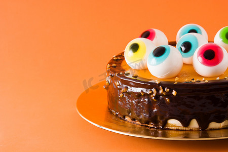 橙色背景中突显的带有糖果眼装饰的万圣节蛋糕