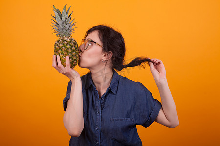 美味菠萝摄影照片_黄色背景中女孩在工作室亲吻美味菠萝的侧视图