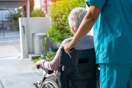 护理人员帮助和护理坐在轮椅上的亚洲老年或老年老妇患者在护理医院的坡道，健康强大的医疗理念。