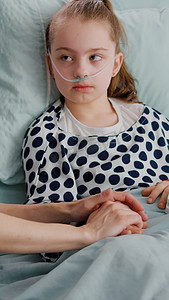 孩子住院摄影照片_戴着氧气鼻管的住院儿童躺在床上，手指上装有医用血氧计
