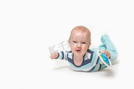 咧着嘴笑的男婴躺在白色背景上，手里拿着一个玩具。