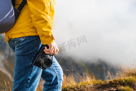 徒步旅行的女人的腿站在云彩覆盖的山峰上拿着相机