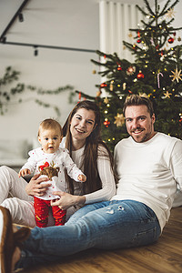 微笑的三口之家圣诞肖像 — 一家人坐在圣诞树前