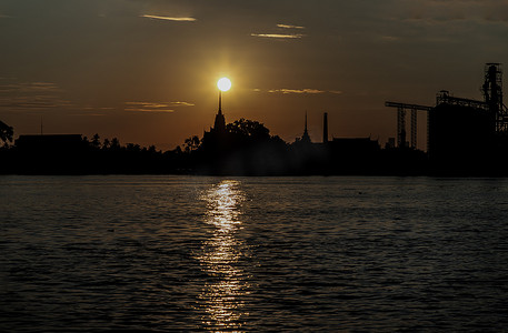 日出时阳光下，泰国寺庙剪影和湄南河沿岸工业工厂的美丽风景。