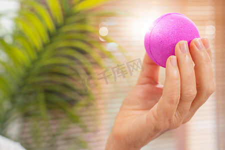 一个女人的手在窗前拿着粉紫色盐和肥皂球的特写镜头。