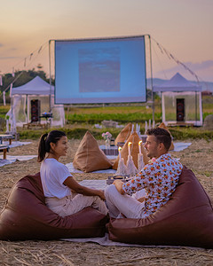 情侣在日落时在外面看电影，晚上在泰国乡村的户外电影院