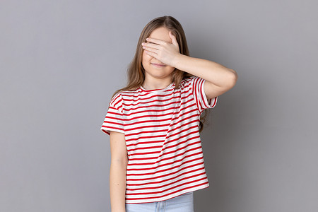 小女孩穿着T恤站着，用手遮住眼睛，拒绝观看，羞愧内容。