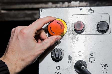 一个男人的手转动旧工业设备控制系统上的红色按钮