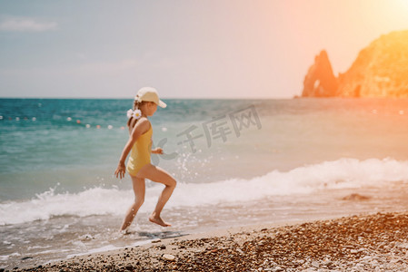 可爱的小女孩沿着海边奔跑，映衬着清澈的蓝色大海，在夏日的阳光下欢欣鼓舞。