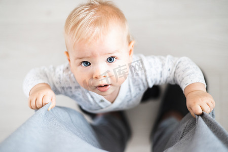 自上而下的视图，快乐的男婴在家里抓住父亲的运动裤迈出了第一步。
