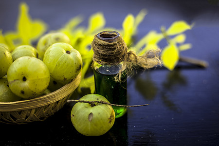 印度醋栗的特写镜头，其提取的精华或浓度在木质表面的透明瓶子中，生醋栗放在水果和蔬菜篮子里。