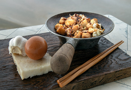 萝卜糕摄影照片_传统的炒软萝卜糕或炒萝卜糕（柴头粿）在小热气腾腾的铁锅里，用木筷子放在白桌上。