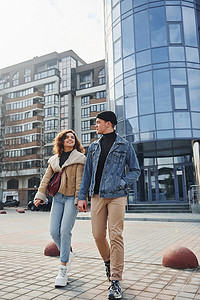 保暖衣服摄影照片_穿着休闲保暖衣服的快乐夫妇在商业大楼附近的城市户外散步