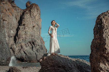 女人白色礼服海石岩石。中年妇女看起来很好，金发，波西米亚风格，穿着白色长裙，脖子和手臂上戴着海滩珠宝。