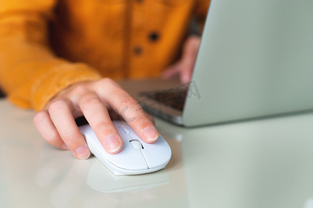 一位身穿衬衫的女商人在电脑上用鼠标工作、坐在办公室的桌子旁或在家工作的特写