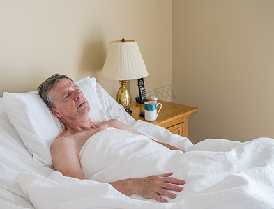 单身白人老人躺在倾斜的床上，躺在明亮的房间里睡着了