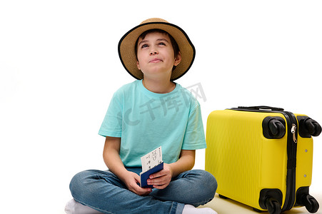 儿童白底摄影照片_帅气的少年旅行者带着登机牌和手提箱，梦幻般地看着一边，出国旅行过周末