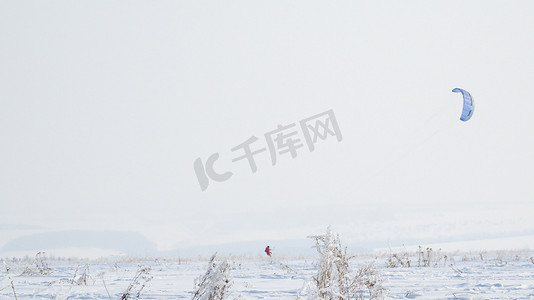 户外裤摄影照片_一个穿着红色连身裤的女孩正在雪地里的冬季滑雪胜地放风筝