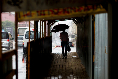一名男子在雨中打着伞行走，脸远离镜头